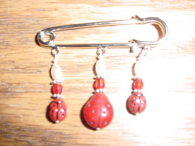 The pin has one large ladybug and two small czech ladybug beads.  There are faux white pearls with sterling silver spacers and head pin.  There is a 4mm ruby red beads in the pin.  The width of the pin is about 1.5 inches.
