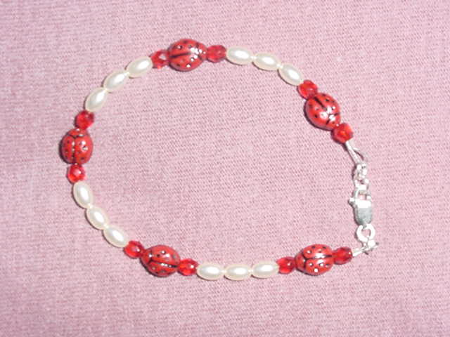 Oval cream ladybug bracelet.  Findings are all of sterling silver.  The wire is stainless steel with plastic coat over it. 